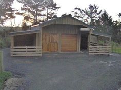 two wooden garages sitting next to each other on a gravel road with trees in the background