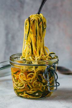 a jar filled with noodles and sauce being held by a black spoon over the top