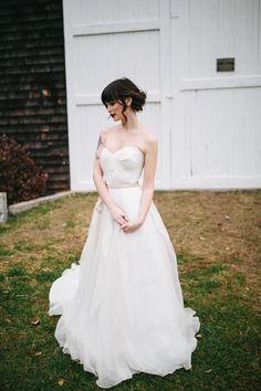 a woman in a white wedding dress standing on the grass near a barn and shed