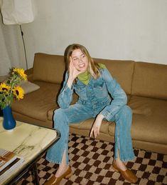 a woman sitting on top of a brown couch next to a vase with yellow flowers