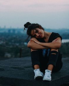 a woman sitting on top of a cement wall next to a sky line with buildings in the background