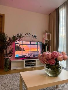 a vase with pink flowers sitting in front of a flat screen tv