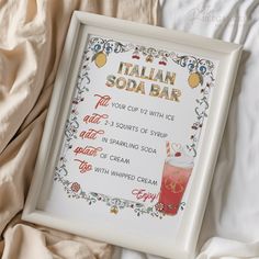 a framed italian soda bar sign sitting on top of a bed next to a blanket