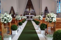 an aisle lined with white flowers and potted plants in front of the pews