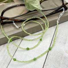 Shiny and bohemian eyeglass necklace chain in green tones with light flashes of gold, made with Preciosa Czech crystal seed beads and tiny green Jade gemstones.     Paired with beautiful silver plated crystal seed beads, this handmade eyeglass chain will definitely create a unique look. This eyeglass lanyard is made on strong quality beading wire with wire guardians that protect the quality eyeglass holder grips. The necklace is ended with spring clasps that hold the eyeglass grips and they can Beaded Green Glasses Chains For The Beach, Beaded Green Glasses Chains For Beach, Adjustable Glass Gemstone Beaded Necklaces, Adjustable Glass Beaded Necklace With Gemstone Beads, Adjustable Glass Gemstone Beaded Necklace, Green Beaded Glass Jewelry, Green Glass Beaded Jewelry, Spiritual Glass Beaded Necklaces With Adjustable Fit, Adjustable Spiritual Glass Beaded Necklaces