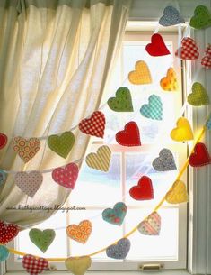 a window with hearts hanging from it's side in front of a white curtain