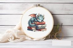 a cross stitch dragon sitting on top of a pile of books