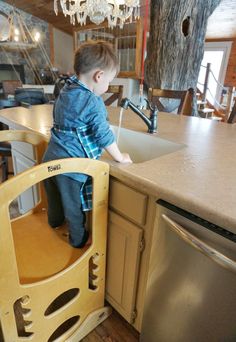 a young boy standing on the edge of a kitchen sink in front of a dishwasher