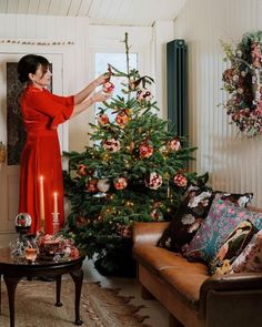 a woman in a red dress decorating a christmas tree