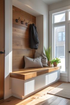 a wooden bench sitting in front of a window next to a plant and coat rack