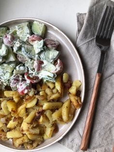 a white plate topped with potato salad next to a fork and knife on top of a napkin