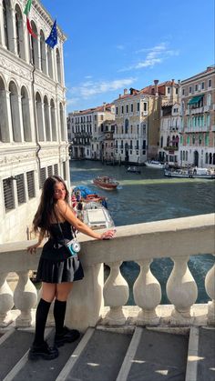 a woman leaning on a railing in front of some buildings and the water behind her