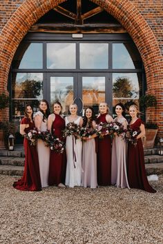 a group of women standing next to each other in front of a brick building holding bouquets