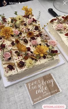 two cakes with flowers on them sitting on a table next to a card and knife