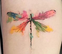 a watercolor dragonfly tattoo on the right side of the thigh, it is painted with multi - colored ink