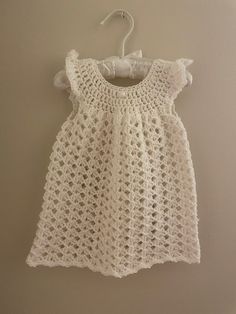 a white crochet dress hanging on a wall with a hanger attached to it