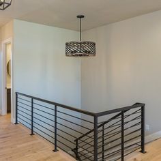 an empty living room with hard wood flooring and metal handrails, along with a chandelier