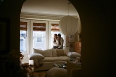 two people standing next to each other in front of a living room with white furniture