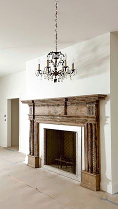 an empty living room with a fireplace and chandelier hanging from the ceiling above it