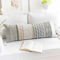 a white couch with a book, cup and vase on it next to an open book