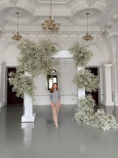 a woman is standing in the middle of a room with flowers hanging from the ceiling