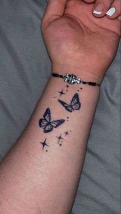 a woman's wrist with two butterflies on it and stars in the sky behind her