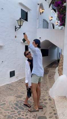 a man and woman standing in front of a white building pointing at something on the wall