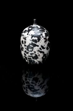 a black and white vase sitting on top of a reflective surface in front of a black background