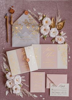 the wedding stationery is laid out with flowers and gold foil