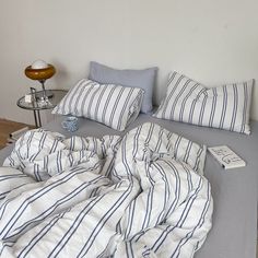 an unmade bed with blue and white striped comforter on top of it next to a lamp