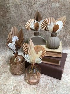 three vases with flowers in them sitting on top of some books and other items