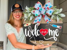 a woman holding up a welcome sign in front of a door with a bow on it