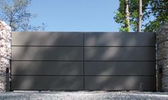 a large gray gate in the middle of a stone wall and tree lined driveway area