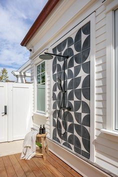 an outdoor shower on a wooden deck next to a white house with black and white tiles