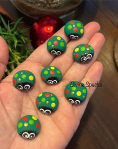 green and red painted rocks with eyes on them in front of a plant, christmas ornament