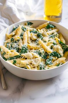 a white bowl filled with pasta and spinach next to a glass of orange juice