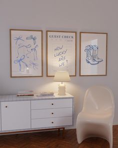 a white chair sitting next to a lamp on top of a wooden floor in front of two framed pictures