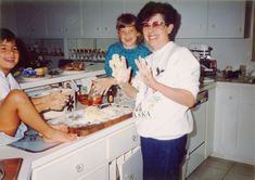 three boys and an older woman are in the kitchen making dough for cookies with their hands