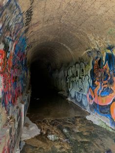 a tunnel with graffiti on the walls and water running through it in an area that looks like a cave