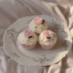 three cupcakes with white frosting and pink flowers on a plate