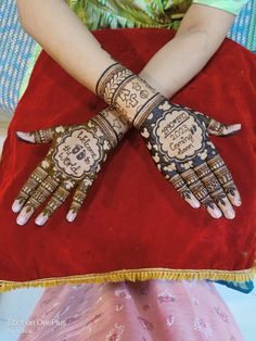 a woman's hands decorated with hennap and writing on the palms, sitting on a red pillow