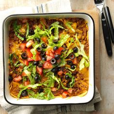 a white casserole dish with black olives, tomatoes and lettuce