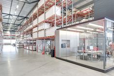 an empty warehouse with glass walls and lots of shelves on each side, including tables and chairs