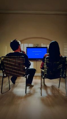 two people sitting in chairs watching a television