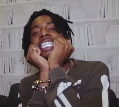 a man with dreadlocks sitting in front of a bookshelf holding his hands to his face