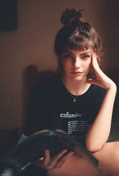 a young woman sitting on the floor with her hand under her head and reading a book