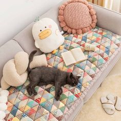 a black cat laying on top of a bed next to pillows and stuffed animals,