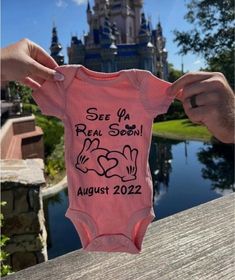 someone holding up a pink onesie with the disney castle in the background