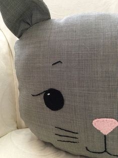 a gray and black cat pillow sitting on top of a white couch next to pillows