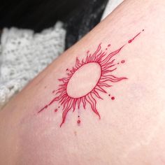 a small sun tattoo on the back of a woman's thigh, with red ink